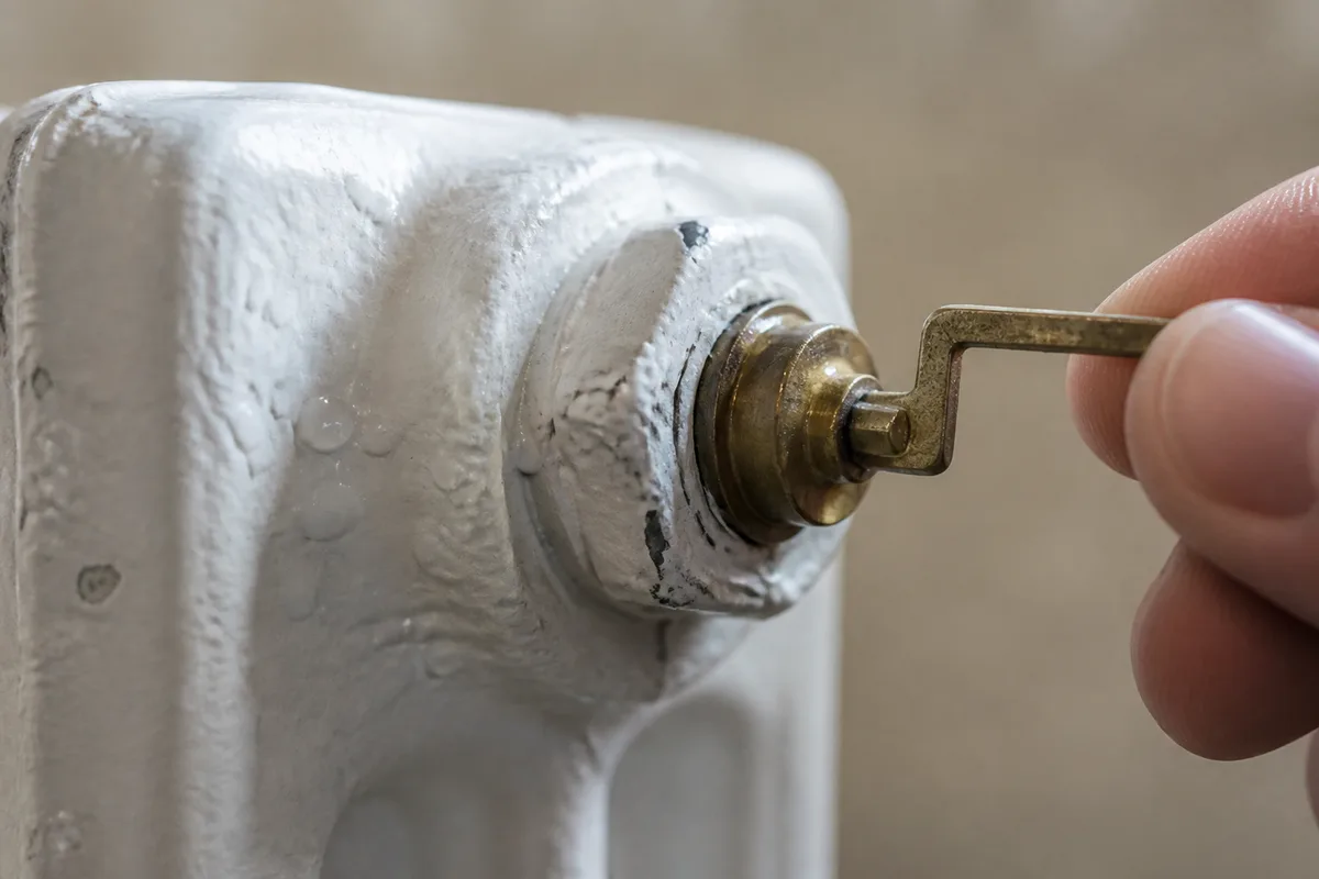 Purgeur de radiateur manipulé avec une clé, mousse et gouttes visibles sur la peinture blanche