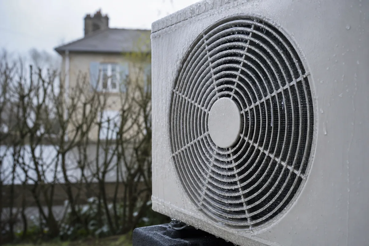 Unité extérieure d&rsquo;une pompe à chaleur air-eau givrée devant un pavillon en pierre du Val de Saône