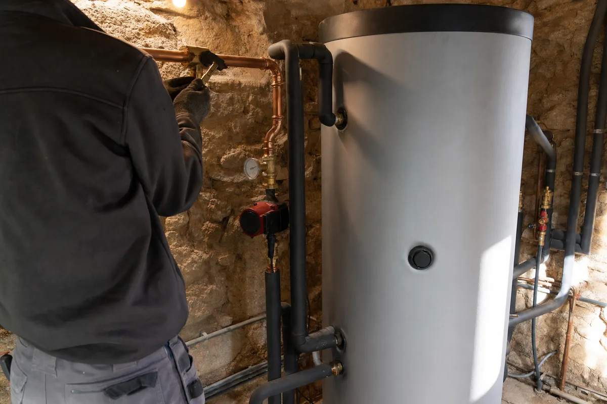 Chaufferie domestique dans une maison de pierre bourguignonne avec ballon solaire, circulateur et tuyauterie cuivre, lumière chaude d’intérieur